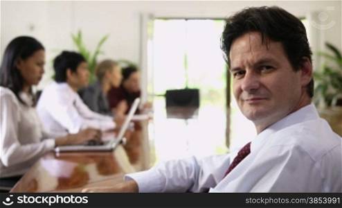 Mature man working as manager and looking at camera during business meeting with employees. Rack focus