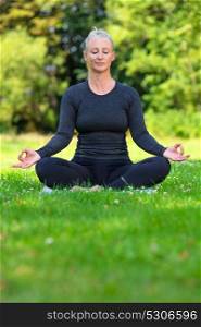 Mature middle aged fit healthy woman practicing yoga kapalbhati pranayama position outside in a natural tranquil green environment