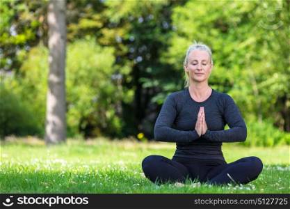 Mature middle aged fit healthy woman practicing yoga outsidein a natural tranquil green environment
