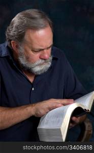 Mature minister with gray beard studies his bible.