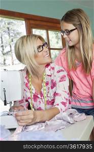 Mature mother looking at daughter while sewing cloth
