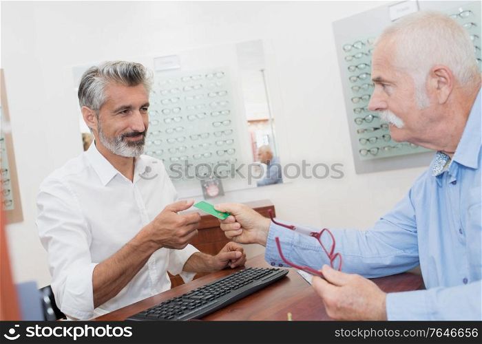 mature optician taking insurance card from senior patient