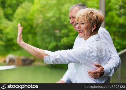 Mature or senior couple at a summer day standing on a bridge waving their hands as if to say goodbye to somebody