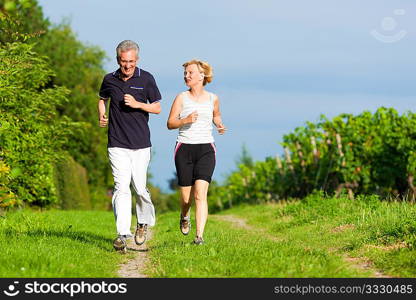 Mature or senior couple doing sport outdoors, jogging down a path in summer