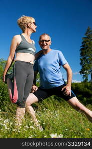 Mature or senior couple in jogging gear doing sport and physical exercise outdoors, stretching and gymnastics