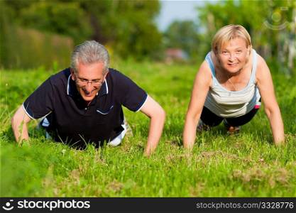 Mature or senior couple in jogging gear doing sport and physical exercise outdoors, pushups