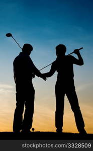 Mature or senior couple playing golf - pictured as a silhouette against an evening sky