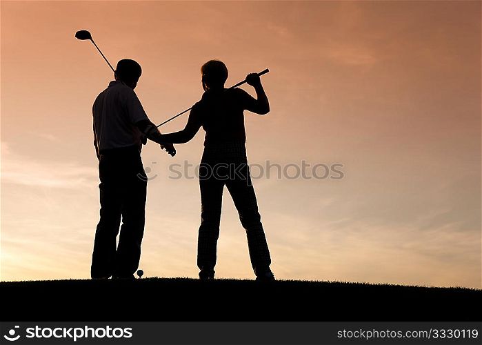 Mature or senior couple playing golf - pictured as a silhouette against an evening sky