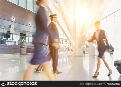 Mature pilot with young beautiful flight attendants walking in airport
