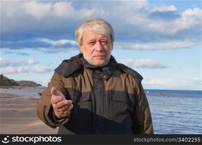 Mature poor man with grey hair at the Baltic sea asks for help in autumn day.