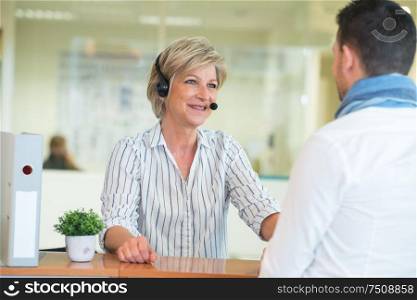mature receptionist wearing headset speaking to customer at counter