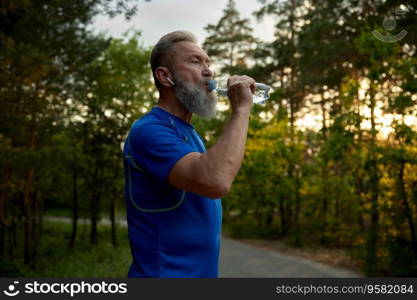 Mature retired man runner taking break drinking water for refreshment during outdoors training in morning. Sport on retirement concept. Mature retired man runner taking break drinking water during training