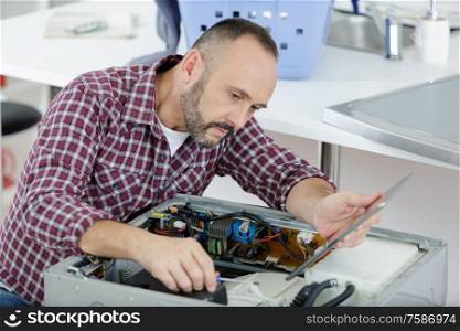 mature serviceman working on appliance and holding tablet