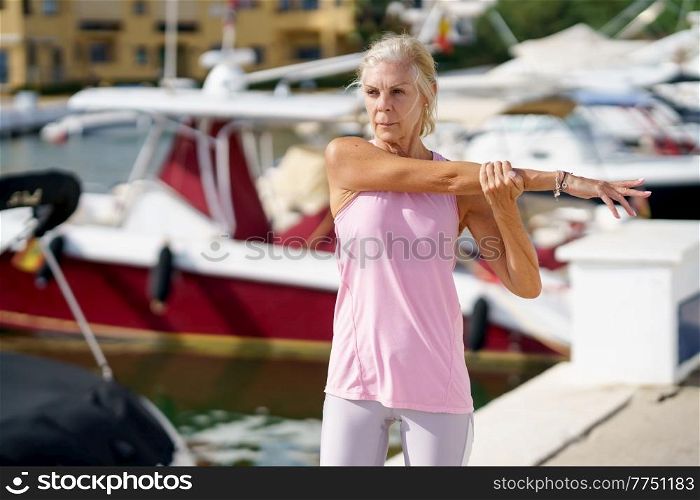 Mature sportswoman stretching her shoulders after exercise. Concept of healthy living in the elderly. Senior woman in fitness clothing. Older female doing sport to keep fit.. Mature woman in fitness clothing stretching her shoulders after exercise.