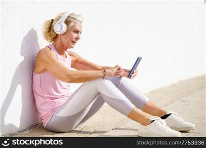 Mature sporty female taking a break to check a fitness app on her smartphone. Senior woman in fitness clothing. Concept of healthy living in the elderly.. Mature sporty woman taking a break to check a fitness app on her smartphone
