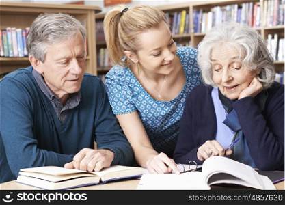 Mature Students Working With Teacher In Library