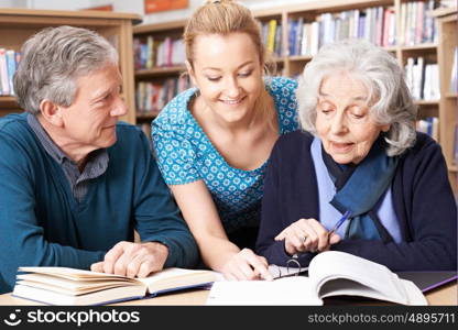 Mature Students Working With Teacher In Library