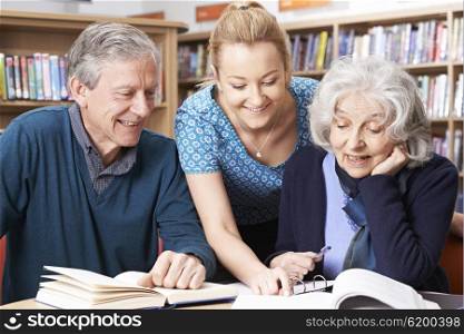 Mature Students Working With Teacher In Library