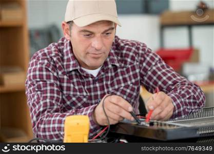 mature technician using multimeter in his workshop