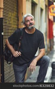 Mature tourist man in urban background. Mature male with white hair and beard wearing casual clothes and travel backpack
