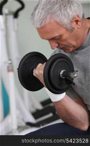 mature white-haired man lifting weight in sports room
