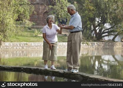 Mature woman afraid of walking on narrow bridge with man at park
