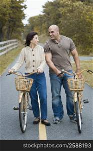 Mature woman and a mid adult man standing with their bicycles and smiling