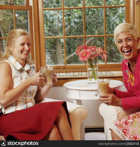 Mature woman and a senior woman holding mugs of coffee and laughing