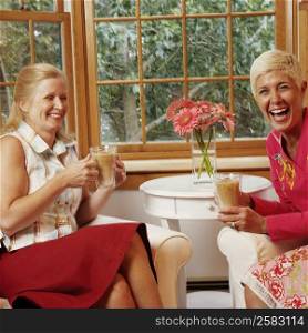 Mature woman and a senior woman holding mugs of coffee and laughing