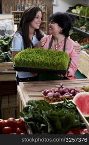 Mature woman and her daughter standing with a tray of wheatgrass in a grocery store and smiling