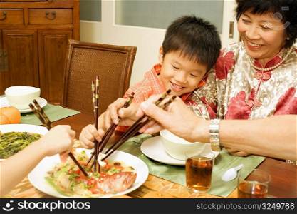 Mature woman and her grandson eating with chopsticks