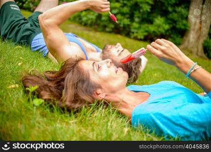 Mature woman and young man lying on grass, eating ice lollies