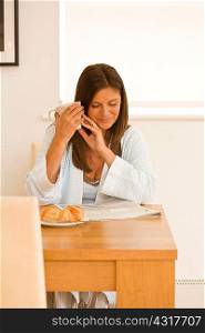 Mature woman at dining table reading newspaper and having breakfast