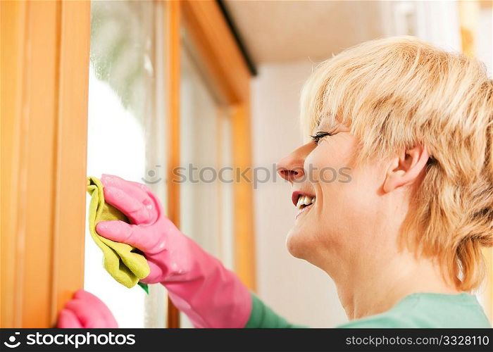 Mature woman cleaning her windows in a spring-clean, she is wearing rubber gloves and looks rather cheerful despite the task