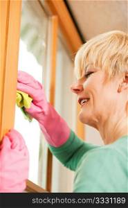 Mature woman cleaning her windows in a spring-clean, she is wearing rubber gloves and looks rather cheerful despite the task