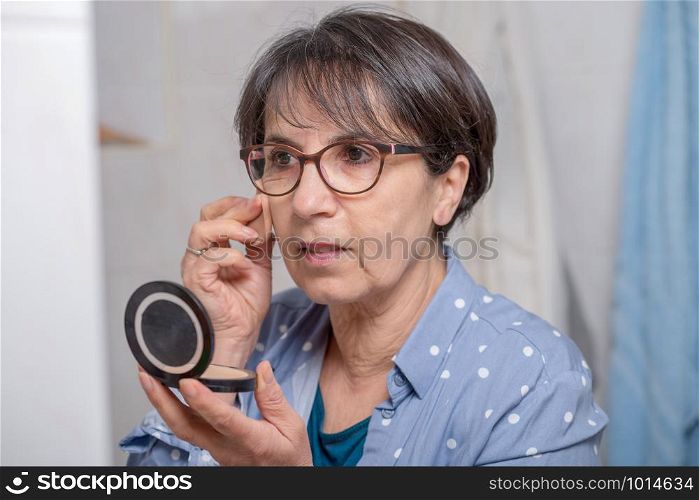 mature woman doing makeup while looking at a small mirror