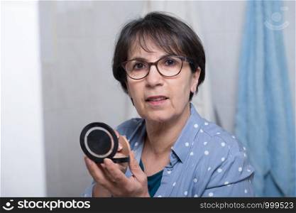 mature woman doing makeup while looking at a small mirror