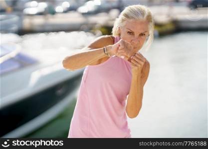 Mature woman doing sport in a coastal port. Arm training throwing boxing punches. Female doing shadow boxing outdoors.. Mature woman doing shadow boxing outdoors. Senior female doing sport in a coastal port