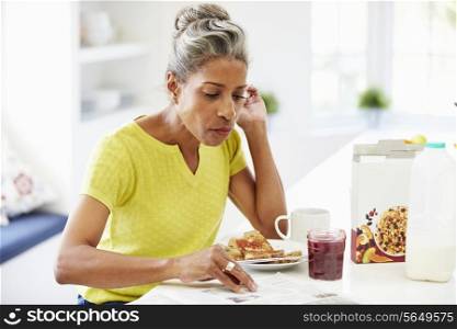 Mature Woman Eating Breakfast And Reading Newspaper
