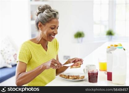 Mature Woman Eating Breakfast Spreading Jam On Toast