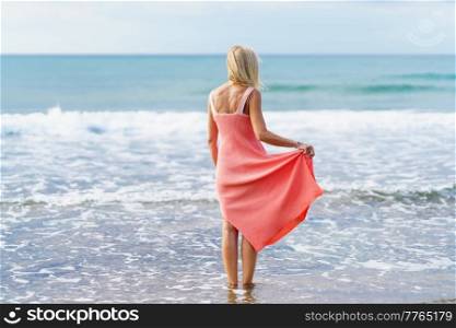 Mature woman enjoying her free time looking at the sea from the shore of the beach.. Elderly female enjoying her retirement at a seaside retreat.. Mature woman enjoying her free time looking at the sea from the shore of the beach.