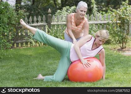 Mature woman exercising on a fitness ball with her sister helping her
