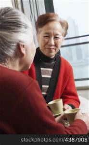 Mature woman facing a senior woman holding a cup of tea