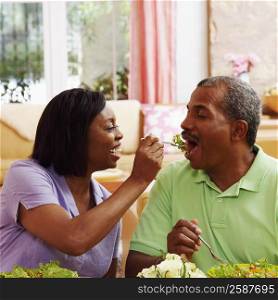 Mature woman feeding salad to a mature man