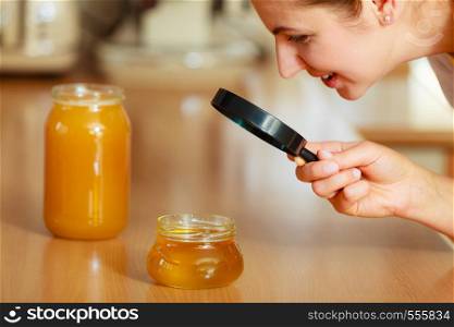 Mature woman female inspecting testing honey food with magnifying glass.. Woman inspecting honey with magnifying glass.