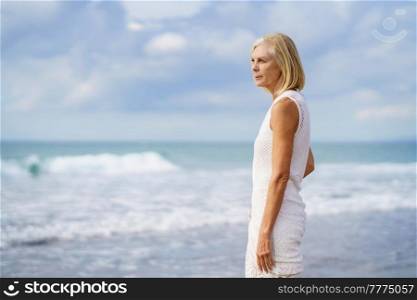 Mature woman gazing serenely at the sea. Elderly female enjoying her retirement at a seaside location.. Mature woman gazing serenely at the sea. Elderly female standing at a seaside location