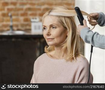 mature woman getting her hair straightened by hairdresser home