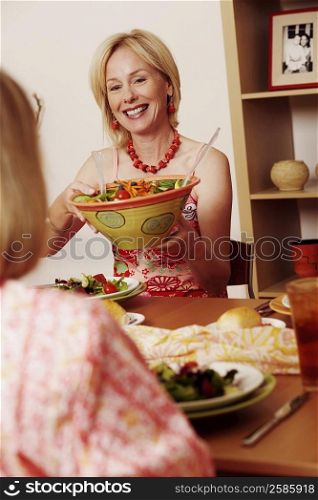 Mature woman giving a bowl of salad to her friend and smiling