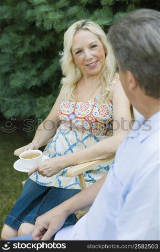 Mature woman holding a cup of tea with a mature man sitting in front of her