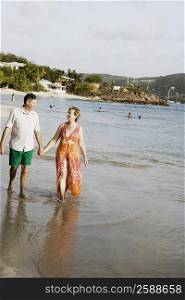 Mature woman holding a senior man&acute;s hand and walking on the beach